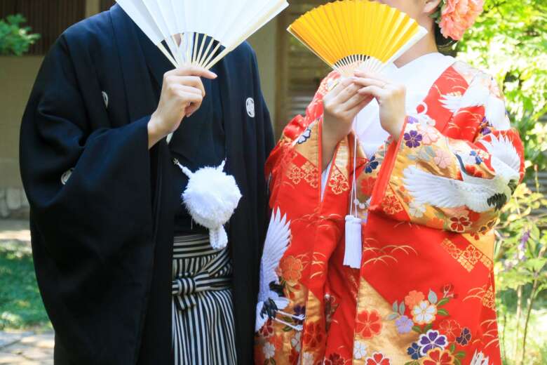 扇子で顔を隠す和装の新郎新婦